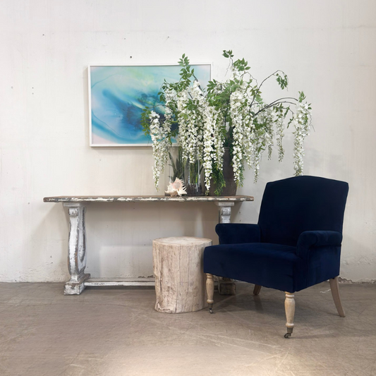 Navy blue armchair in a room with a decorative table, floral arrangement, and abstract painting.